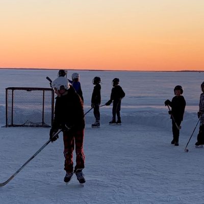 A group of youth playing hockey in the snow while the sun is setting