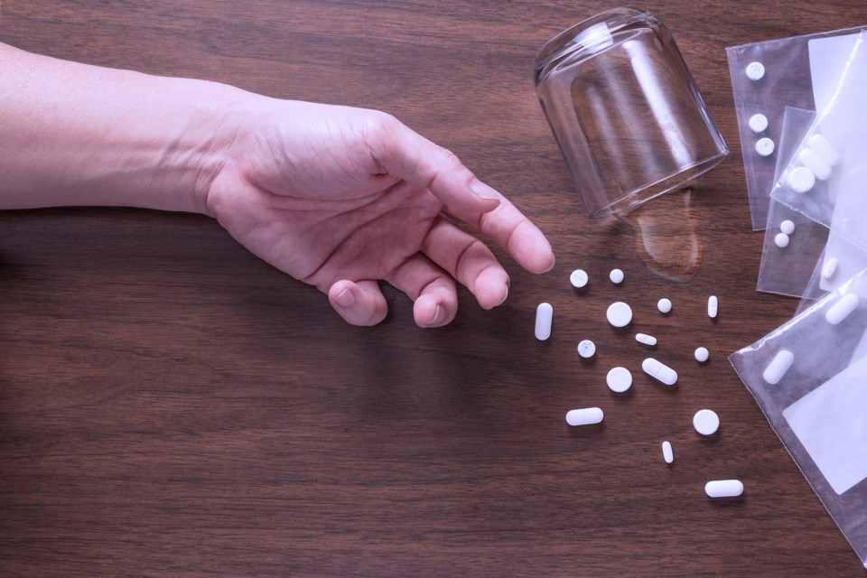 a hand with pills scattered on a table and a glass spilling some water