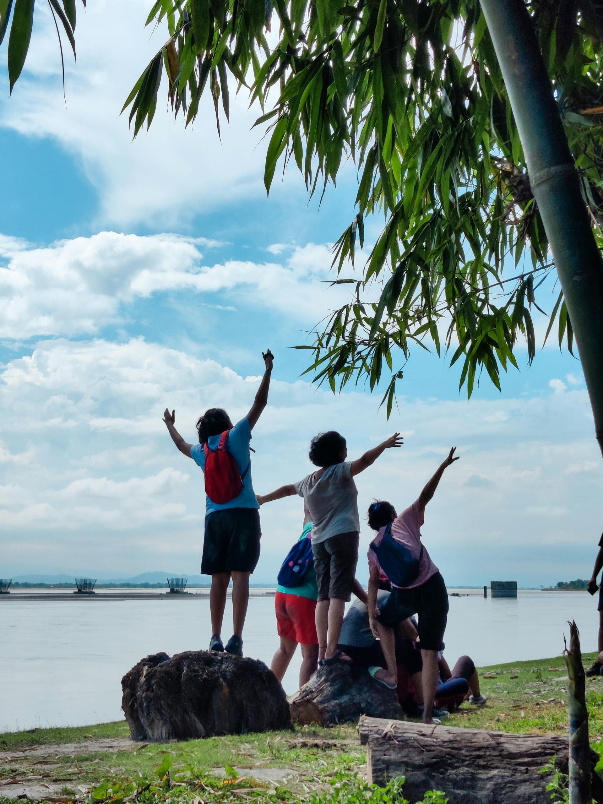 A lively group of friends posing near a serene lake, under a sunny sky, exuding joy and adventure.